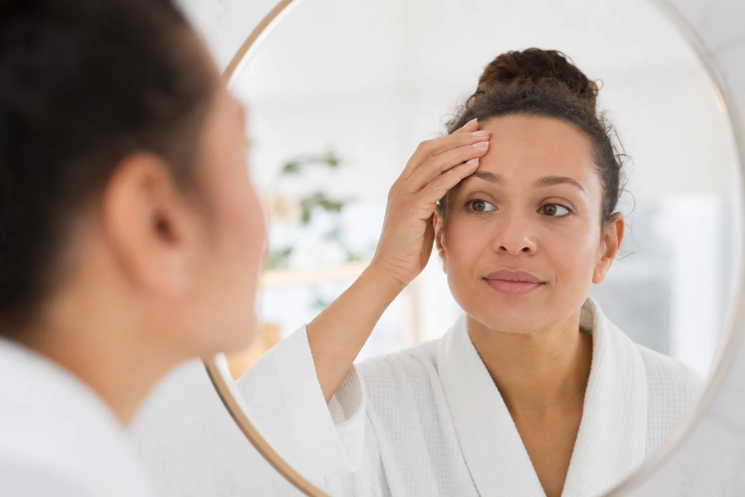 Woman examining her relaxed forehead lines in a mirror while considering treatment options