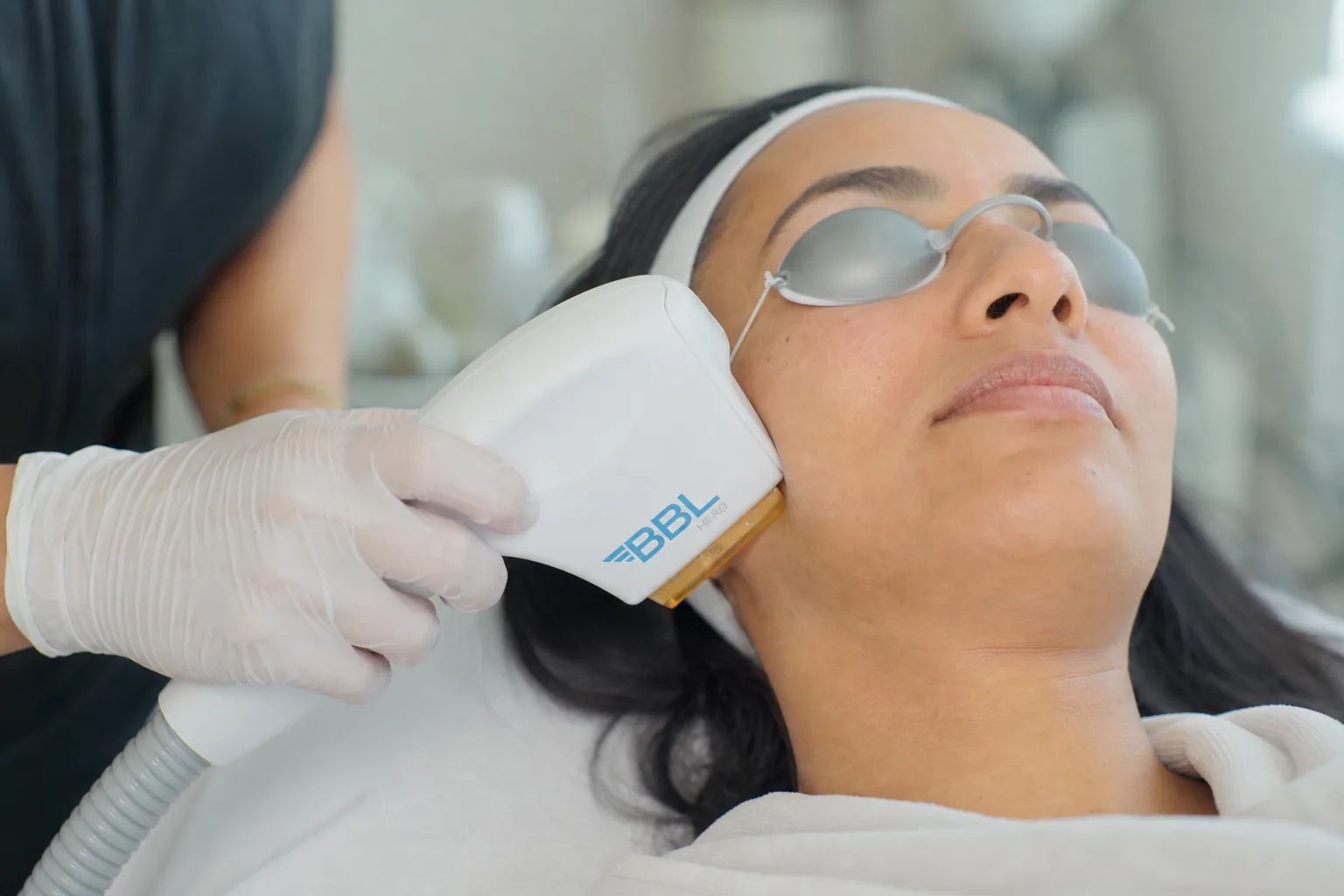 Practitioner's hands gently performing an IPL treatment on a client's cheek in a calm clinic